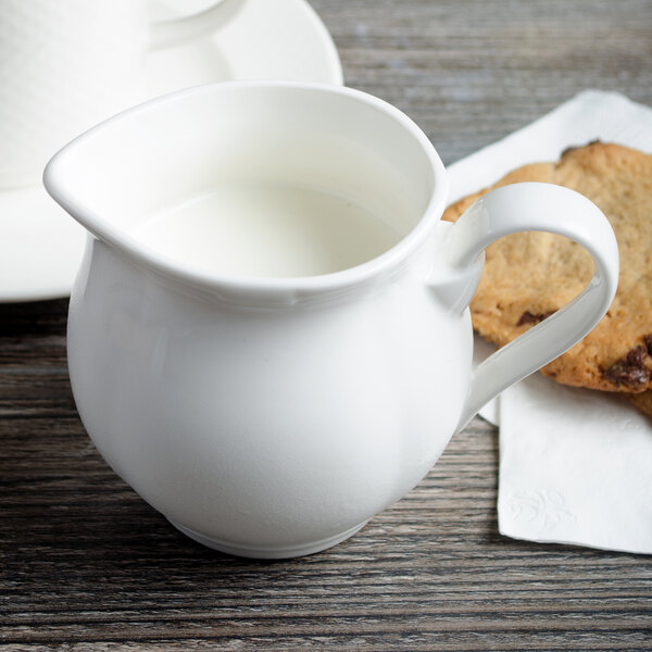 A white Villeroy & Boch porcelain creamer with a handle next to a cookie.