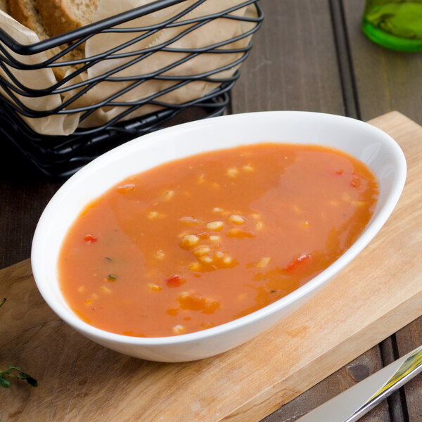 A bowl of soup with bread in a basket on a wood surface.