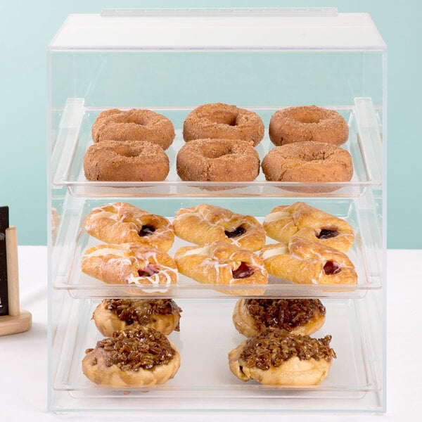 A Cal-Mil three tier acrylic display case filled with pastries on a table.