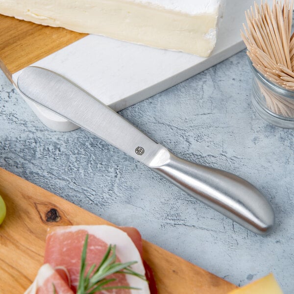 An American Metalcraft stainless steel cheese spreader with soft cheese on it.