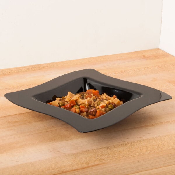 A black Fineline disposable plastic bowl filled with food on a table.