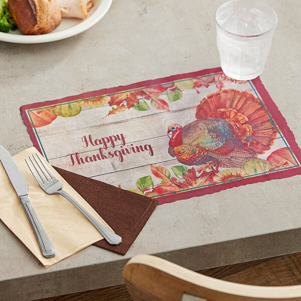 A wooden table set with a Hoffmaster Thanksgiving place mat with a turkey and silverware.