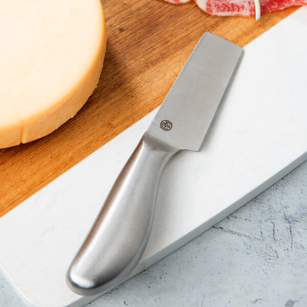 An American Metalcraft Evolution stainless steel cheese knife on a cutting board with cheese and meat.