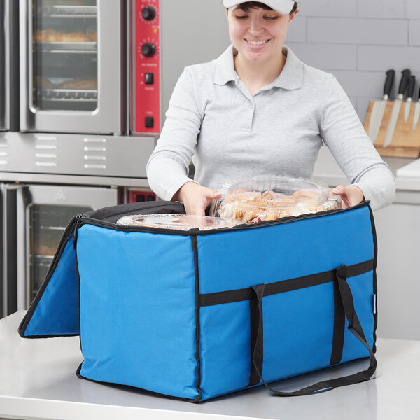 A woman holding a blue Choice insulated food delivery bag with a tray of food inside.