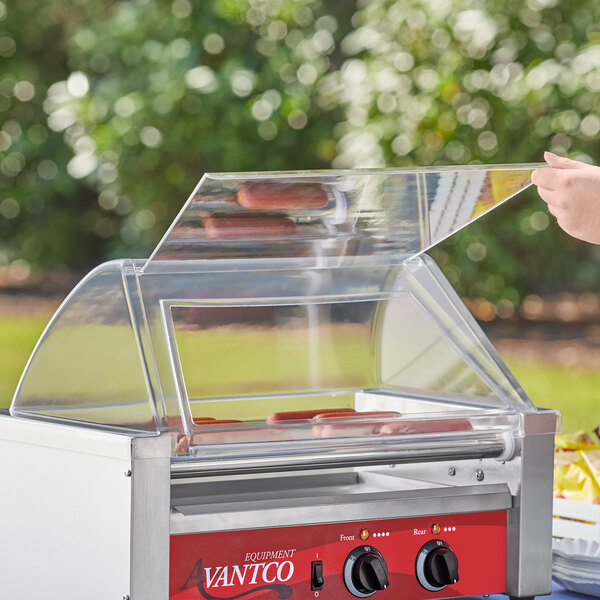 A person using an Avantco hot dog roller grill to cook hot dogs.