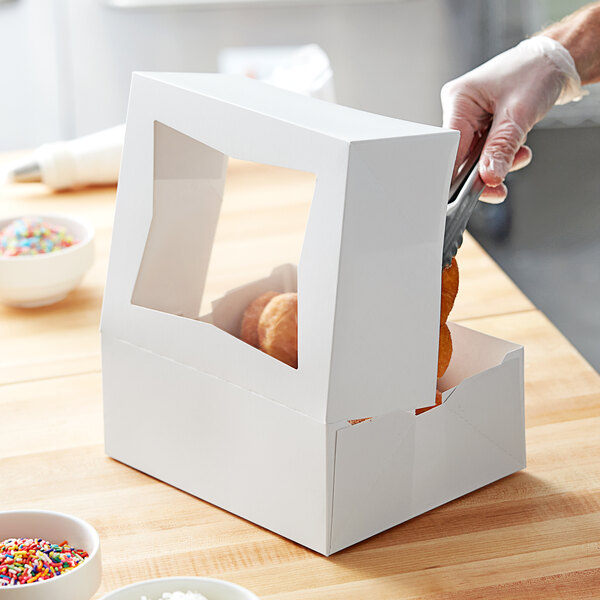 A person cutting a donut in a white Baker's Mark bakery box.