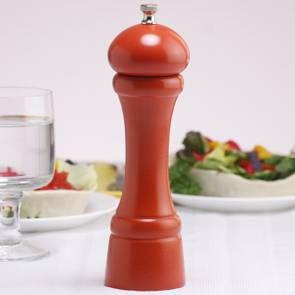 A Chef Specialties butternut orange pepper mill on a table next to a plate of salad.