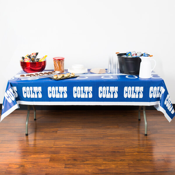 A table with a Creative Converting Indianapolis Colts table cover on it with food.