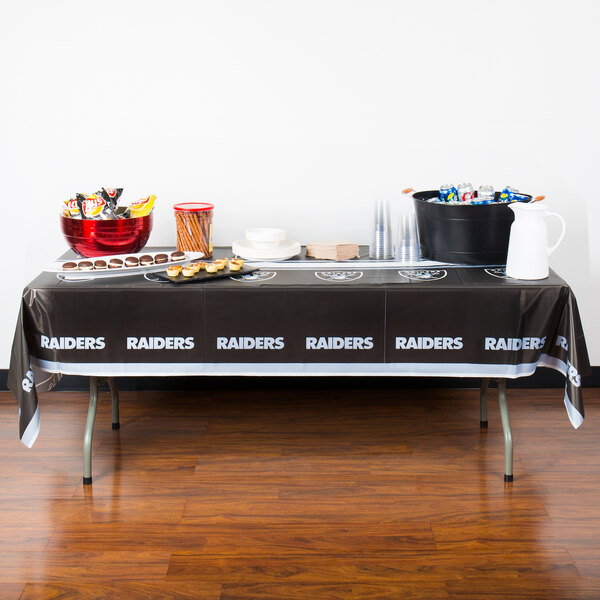 A Creative Converting Las Vegas Raiders plastic table cover on a table with food on it.