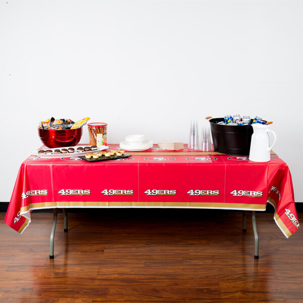 A table with a San Francisco 49ers tablecloth with food and drinks on it.