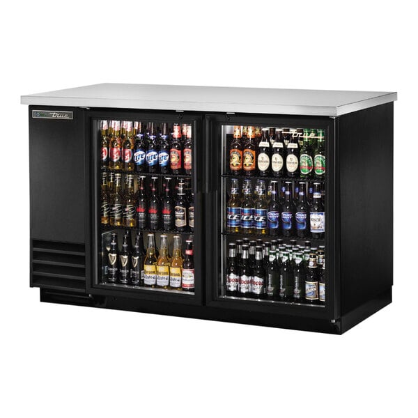 A black True back bar refrigerator with two glass doors filled with bottles of beer.