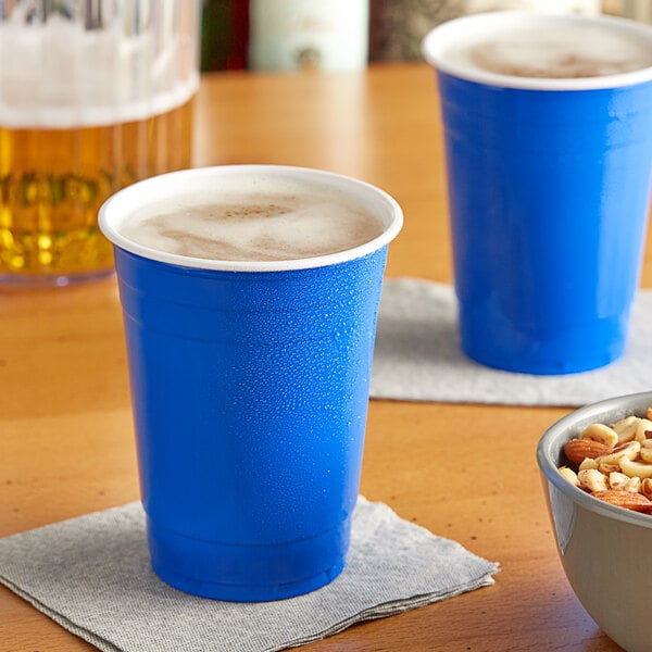 Two blue Choice plastic cups filled with beer on a table with a bowl of nuts.
