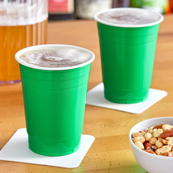 Two green plastic cups with foamy drinks and nuts on a table.