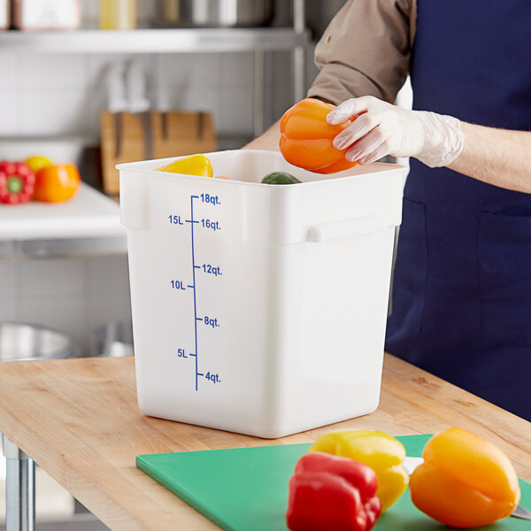 A person putting a yellow bell pepper into a white Choice square food storage container.