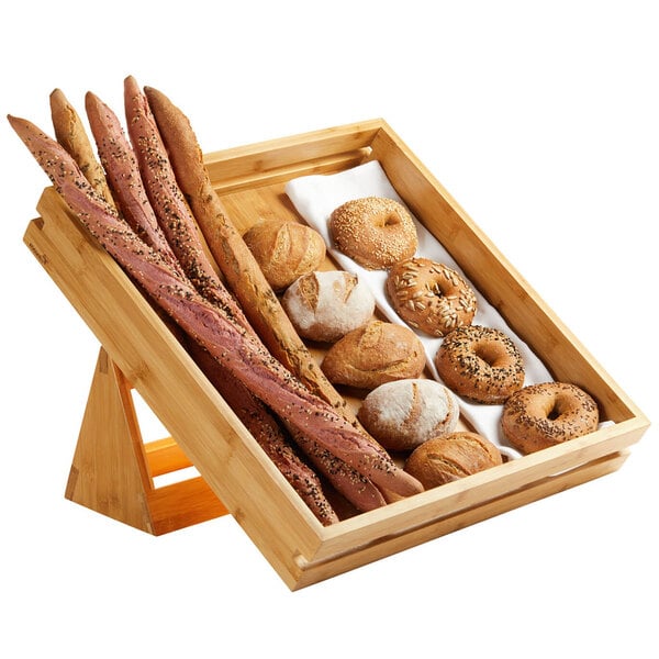 A wooden tray with bread sticks, bagels, and a loaf of bread on it with seeds on the bread sticks.