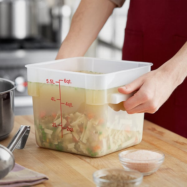 A person holding a Choice translucent square polypropylene food storage container with soup in it.