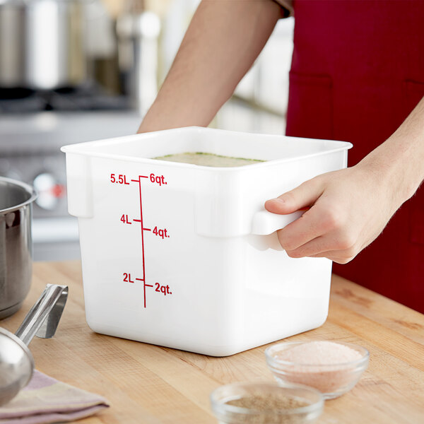 A hand holding a white Choice food storage container with soup in it.