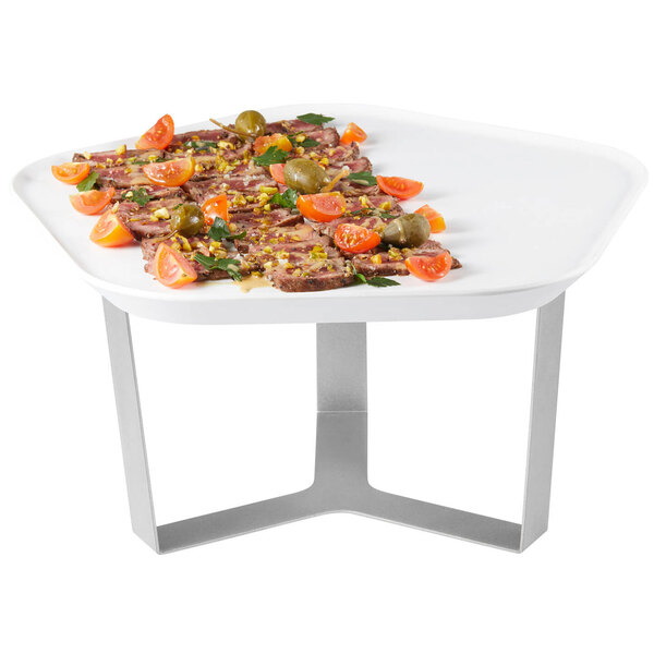 A white polygon tray with food on a white surface on a metal stand.