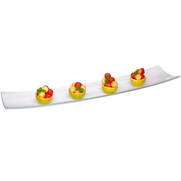 A Rosseto clear narrow rectangular glass platter with a bowl of fruit including watermelon and melon on it.