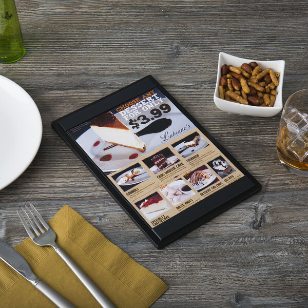 A customizable wood menu board on a table with a menu and utensils.