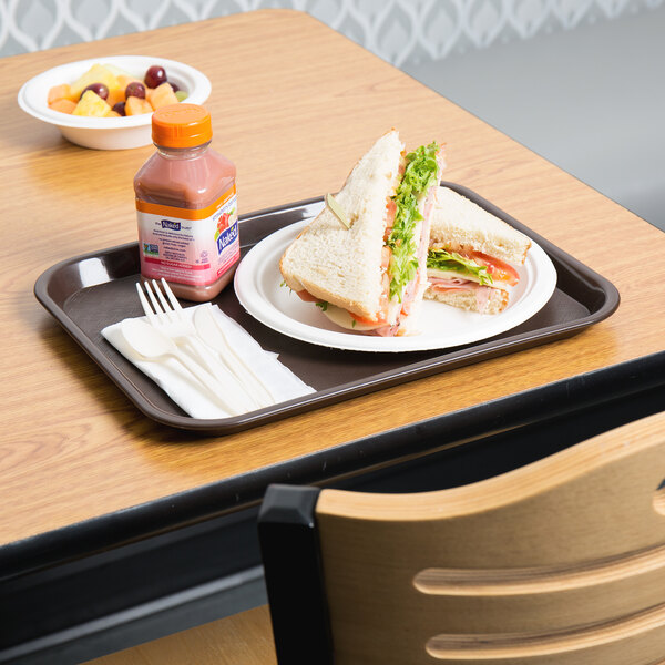 A Choice chocolate brown plastic fast food tray with a sandwich and a bottle of juice on a table.