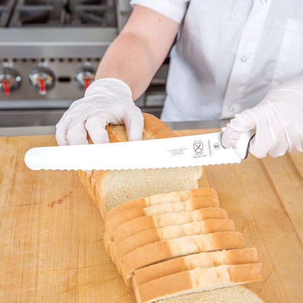A person cutting bread with a Mercer Culinary Millennia bread knife.