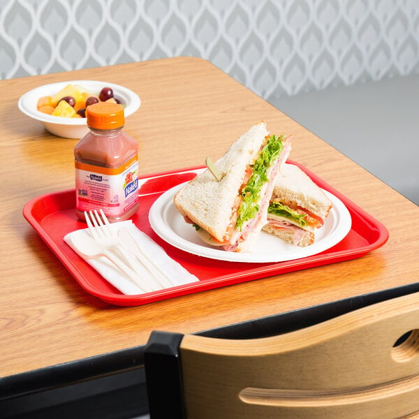 A sandwich and a bottle of juice on a red plastic fast food tray.