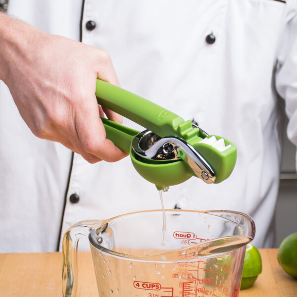A person using a Chef'n FreshForce lime juicer to squeeze lime juice into a measuring cup.