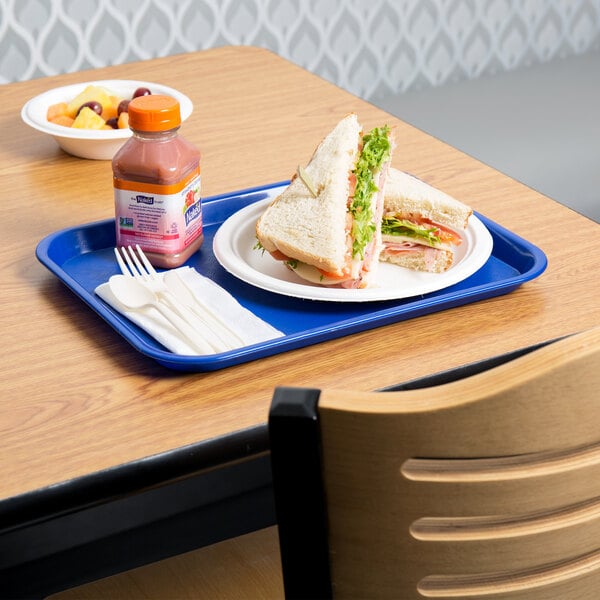 A blue plastic fast food tray with a sandwich, drink, and napkin on a table.