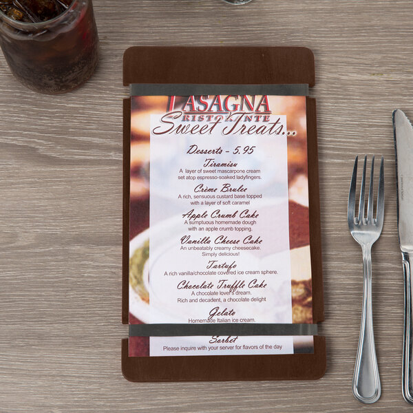 A Menu Solutions customizable wood menu board with rubber band straps on a table with a fork and knife.