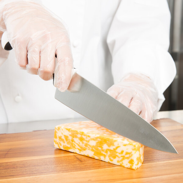 A person cutting a block of cheese on a wooden cutting board with a Mercer Culinary Millennia Chef Knife.