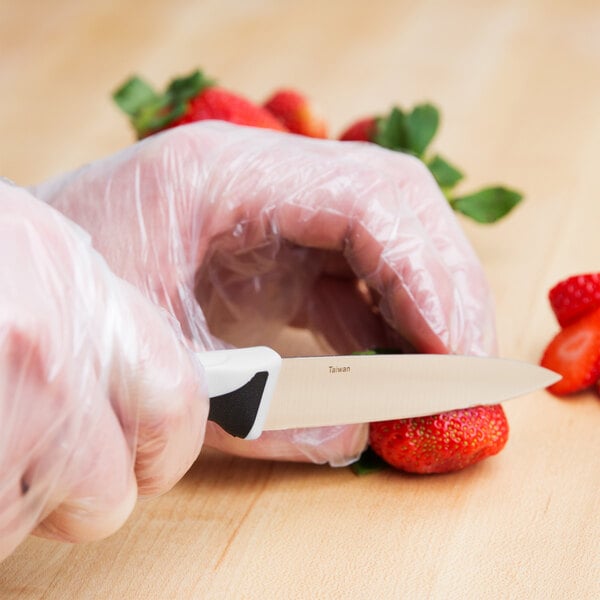 A person in plastic gloves using a Mercer Millennia paring knife to cut a strawberry.