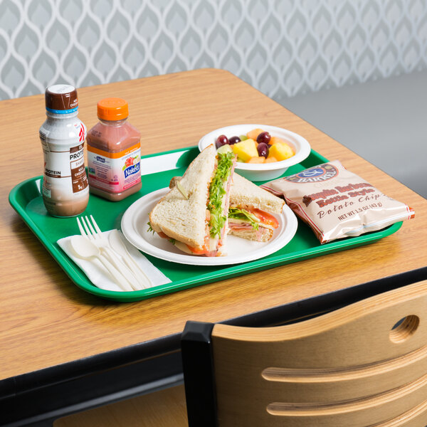 A green plastic Choice fast food tray holding a sandwich and fruit on a table.