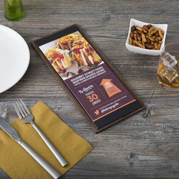 A customizable wood menu board with top and bottom strips on a table with a fork and knife on a napkin.