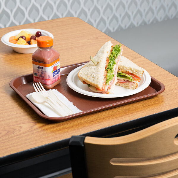 A burgundy plastic fast food tray with a sandwich and a bottle of juice on it.