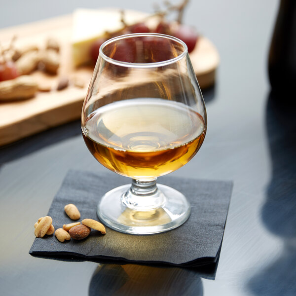 An Anchor Hocking brandy glass filled with liquid on a napkin with nuts.