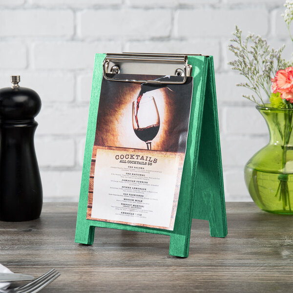 A Menu Solutions teal wood sandwich menu board tent with a clip on a table with a menu on it.