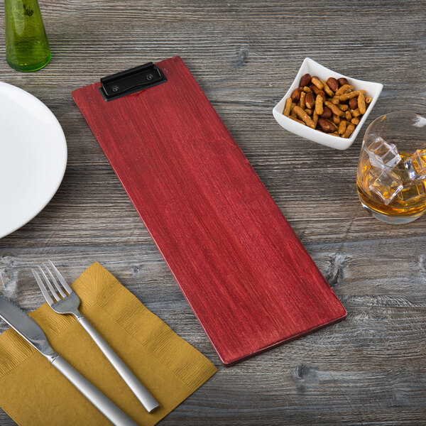 A red rectangular wooden Menu Solutions wood clip board with a white plate and silverware on a wooden table.