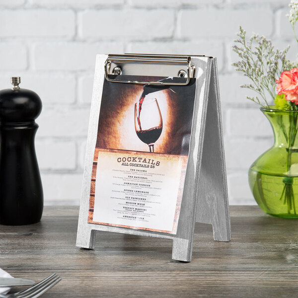 A Menu Solutions white wash wood sandwich menu board tent with a clip holding a menu on a table.