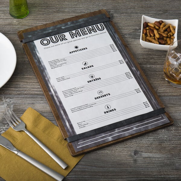 A customizable wood menu board with rubber band straps on a table with a menu, fork, and knife.