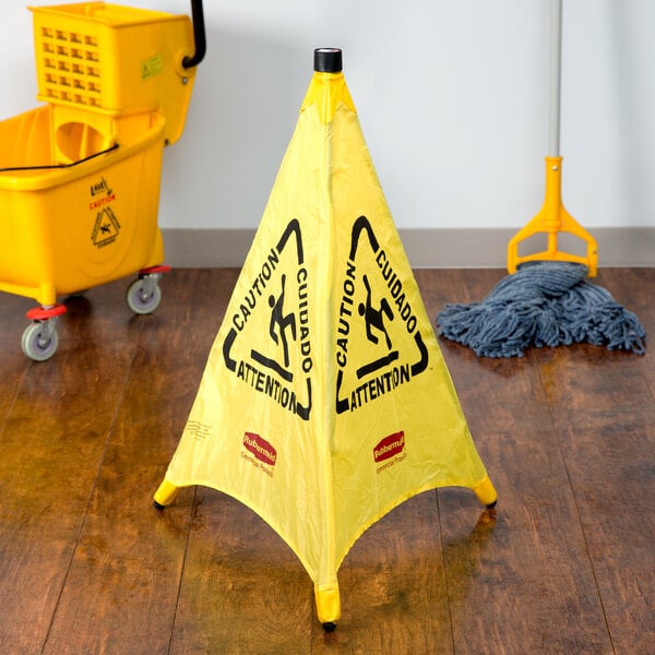 A yellow Rubbermaid "Caution" wet floor sign cone on a wood floor.
