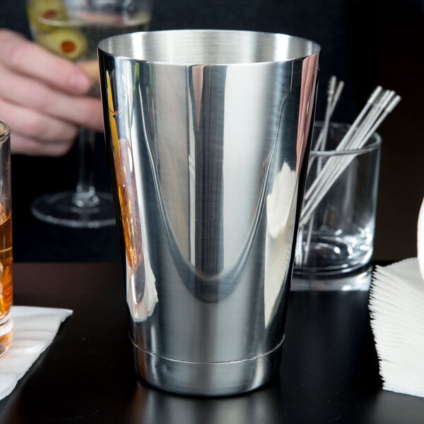 A close-up of a silver Barfly cocktail shaker tin on a table.