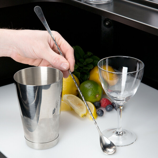 A hand holding a Barfly stainless steel Japanese style bar spoon next to a silver cup.