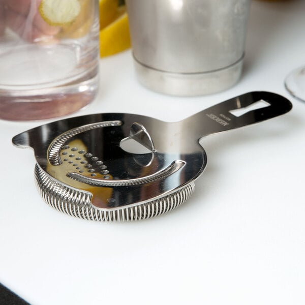 A Barfly stainless steel Hawthorne strainer on a counter.