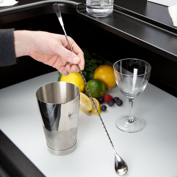 A hand using a Barfly Japanese style bar spoon to mix a drink in a silver cup with a lime slice.