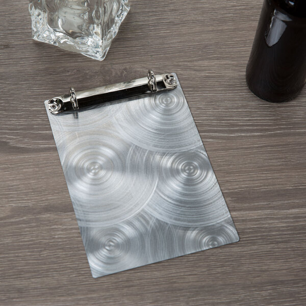 A Menu Solutions Alumitique aluminum menu board with metal swirl finish rings on a table with a glass of beer.