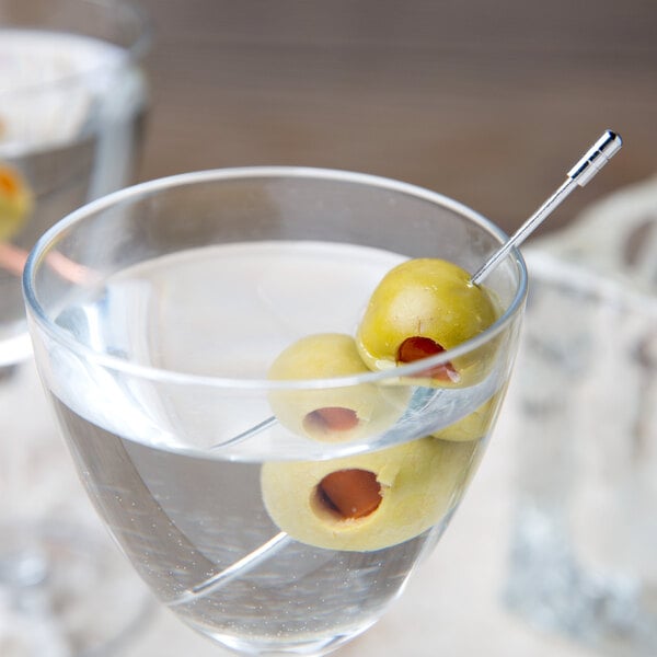 A martini glass with a Barfly stainless steel cocktail pick holding olives in it.