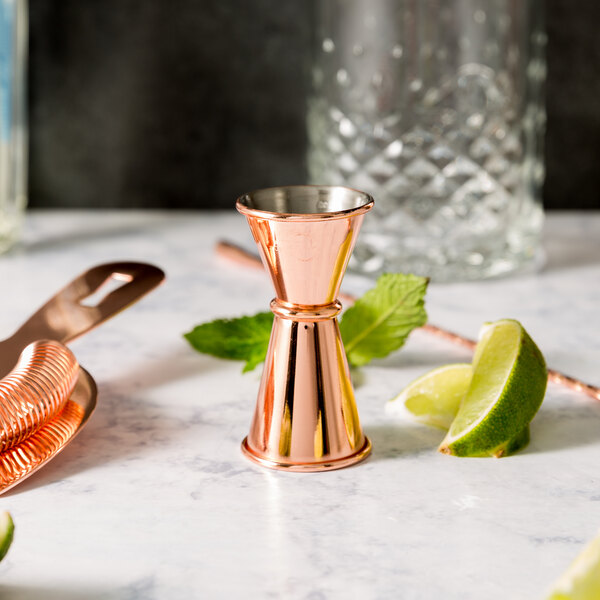 A Barfly copper jigger on a marble surface with limes.