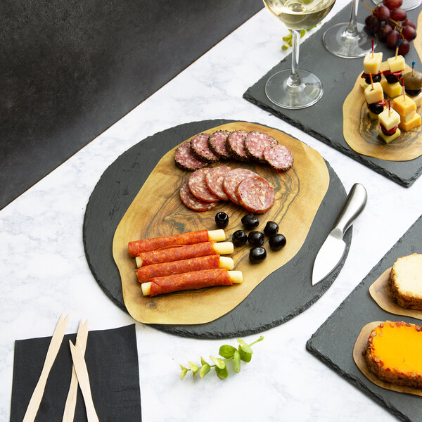 A round black slate tray used for serving food, shown here with assorted meats, cheese sticks, and olives.
