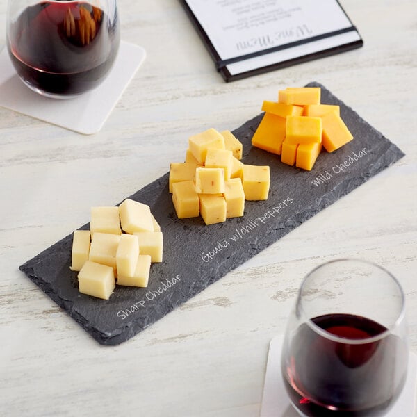Acopa black slate tray with cheese and wine on a table.